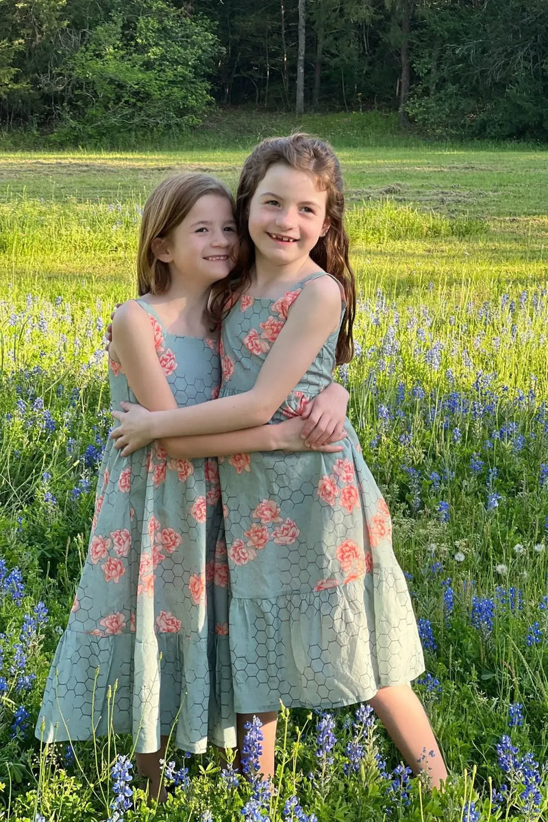 Two girls in matching honeycomb floral dresses stand in a field of bluebonnets.