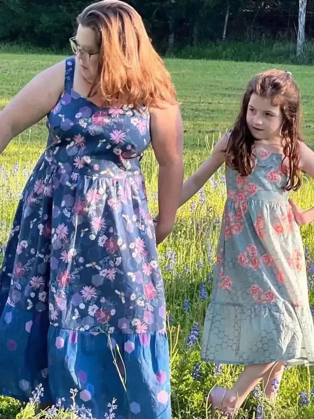 Purple fabric with garden bees print, shown in a flowing dress on a woman and girl in a field.