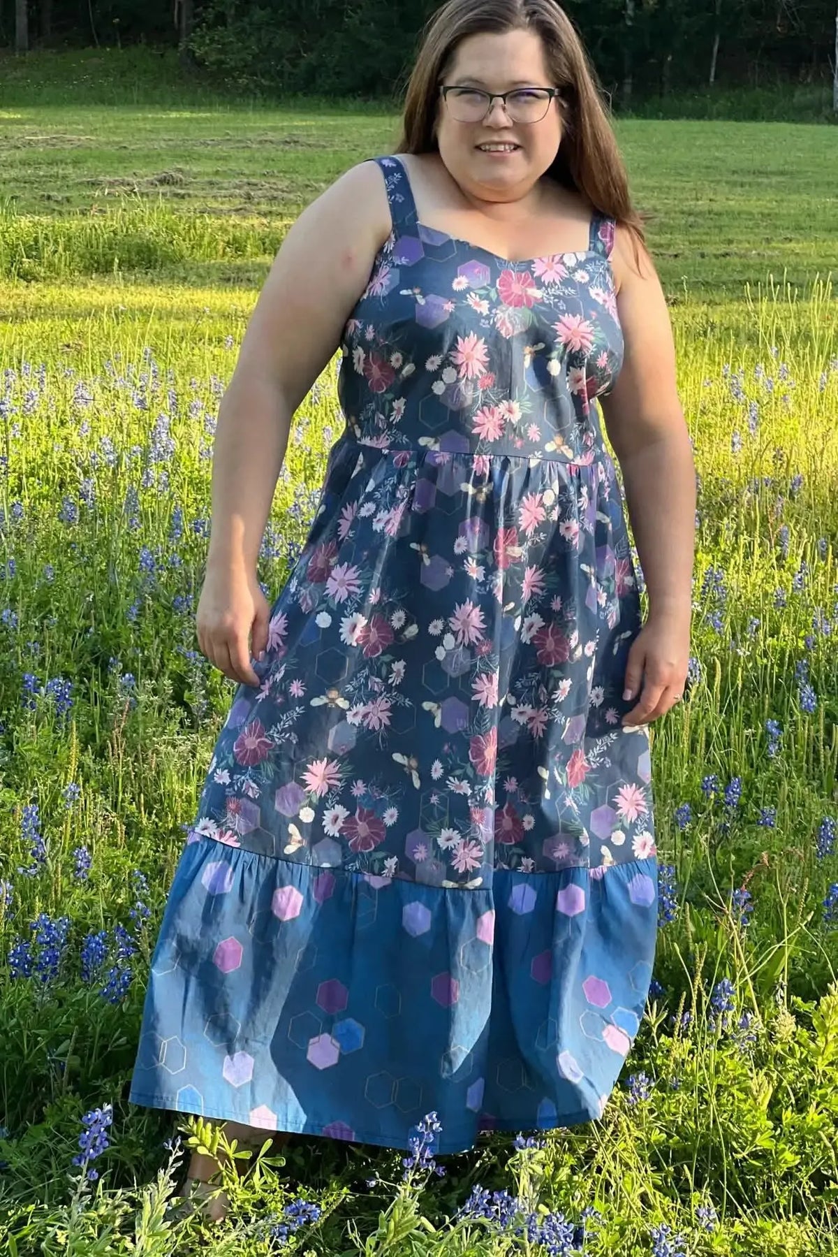 A woman in a floral and geometric print dress stands in a field of blue flowers.