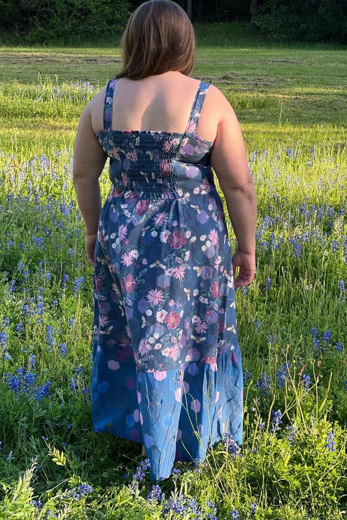 A person from behind wears a floral and geometric patterned dress in a field of bluebonnets.