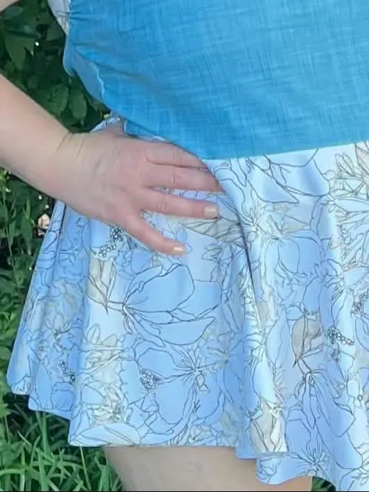 A person wears a blue top and a light blue floral skirt.