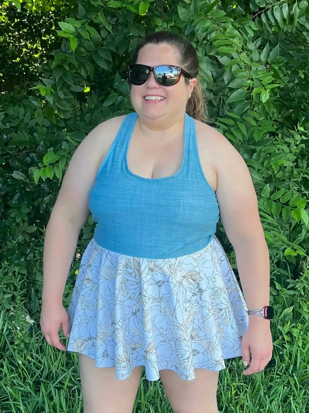 A woman wears a blue tank top and a white floral skirt with a nature sketch pattern.