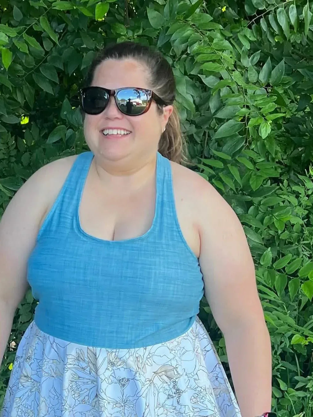 A woman wears a light blue tank top and a white floral skirt.