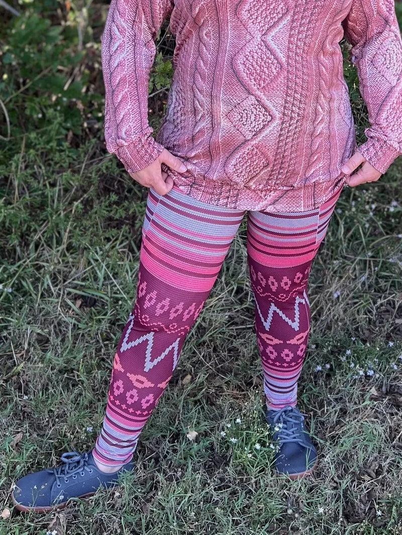 A person wears a pink sweater and patterned leggings with dark shoes.