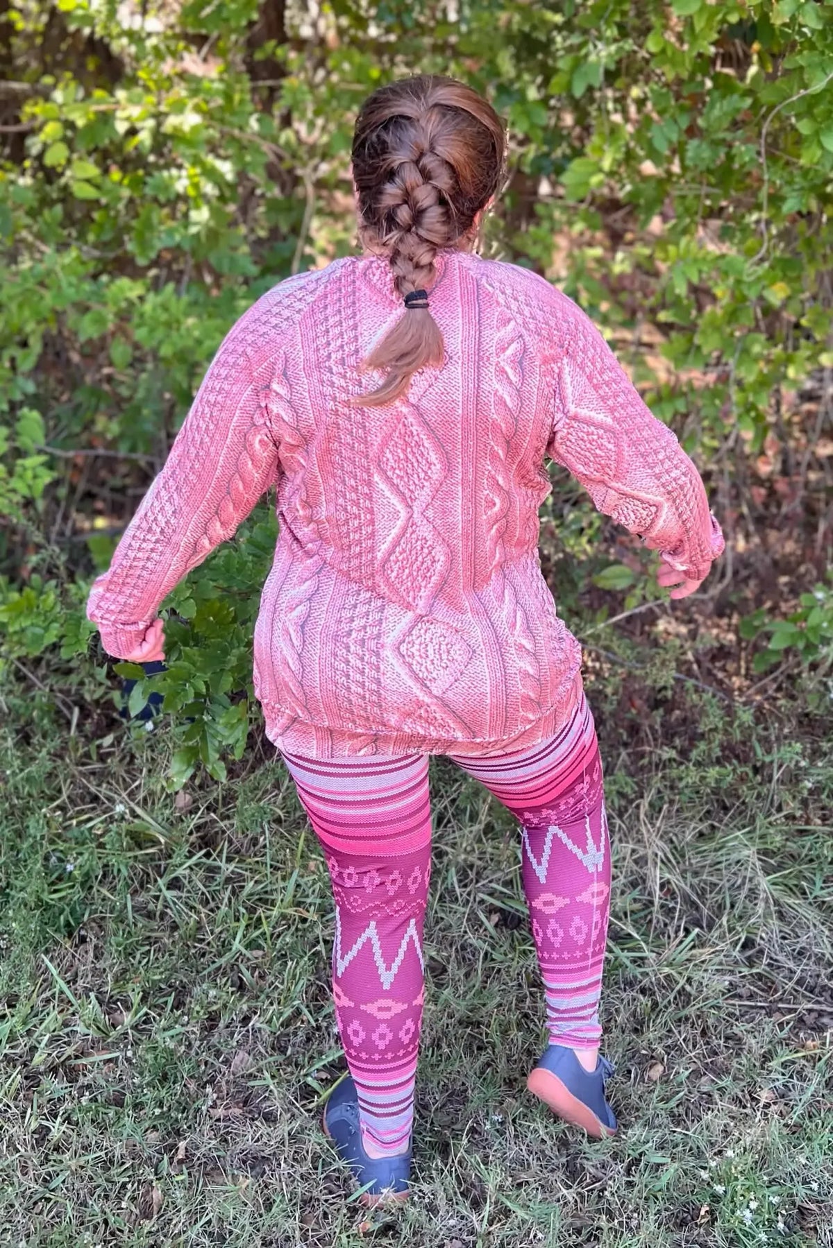 A person from behind wearing a pink cable knit sweater and patterned leggings.