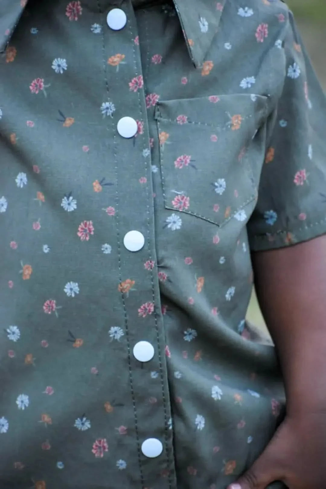 Close-up of an olive green floral print shirt with white buttons and a pocket.