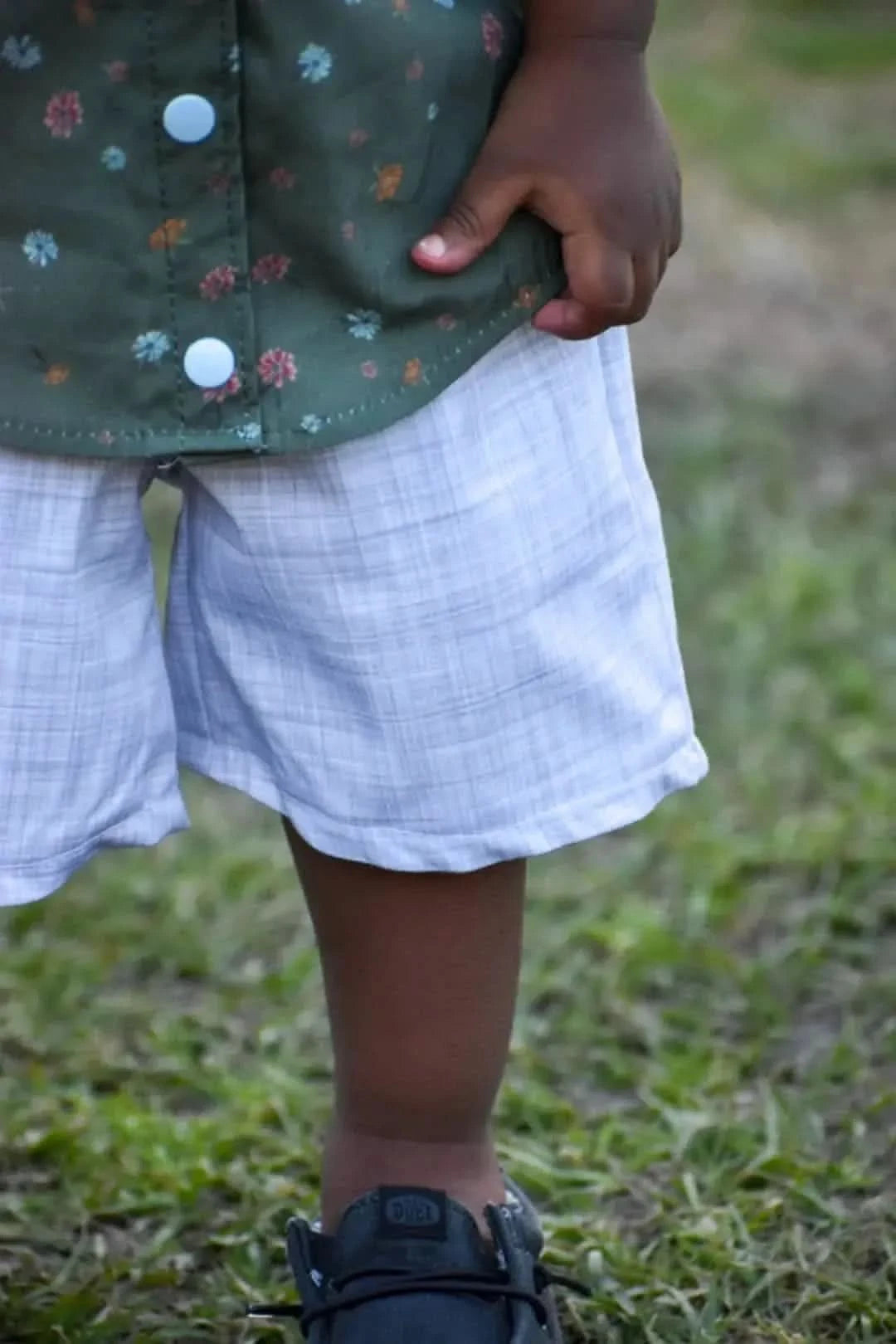 A child wears an olive floral shirt with light blue buttons and light blue plaid shorts.