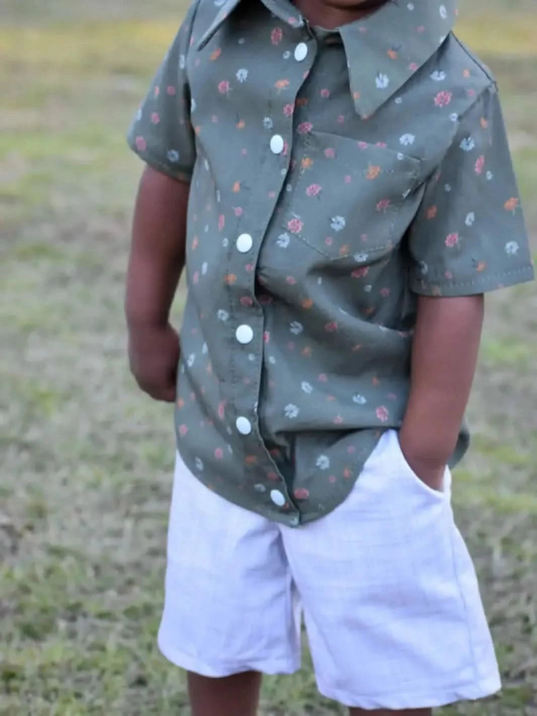 Child in olive floral shirt with white buttons and white shorts.