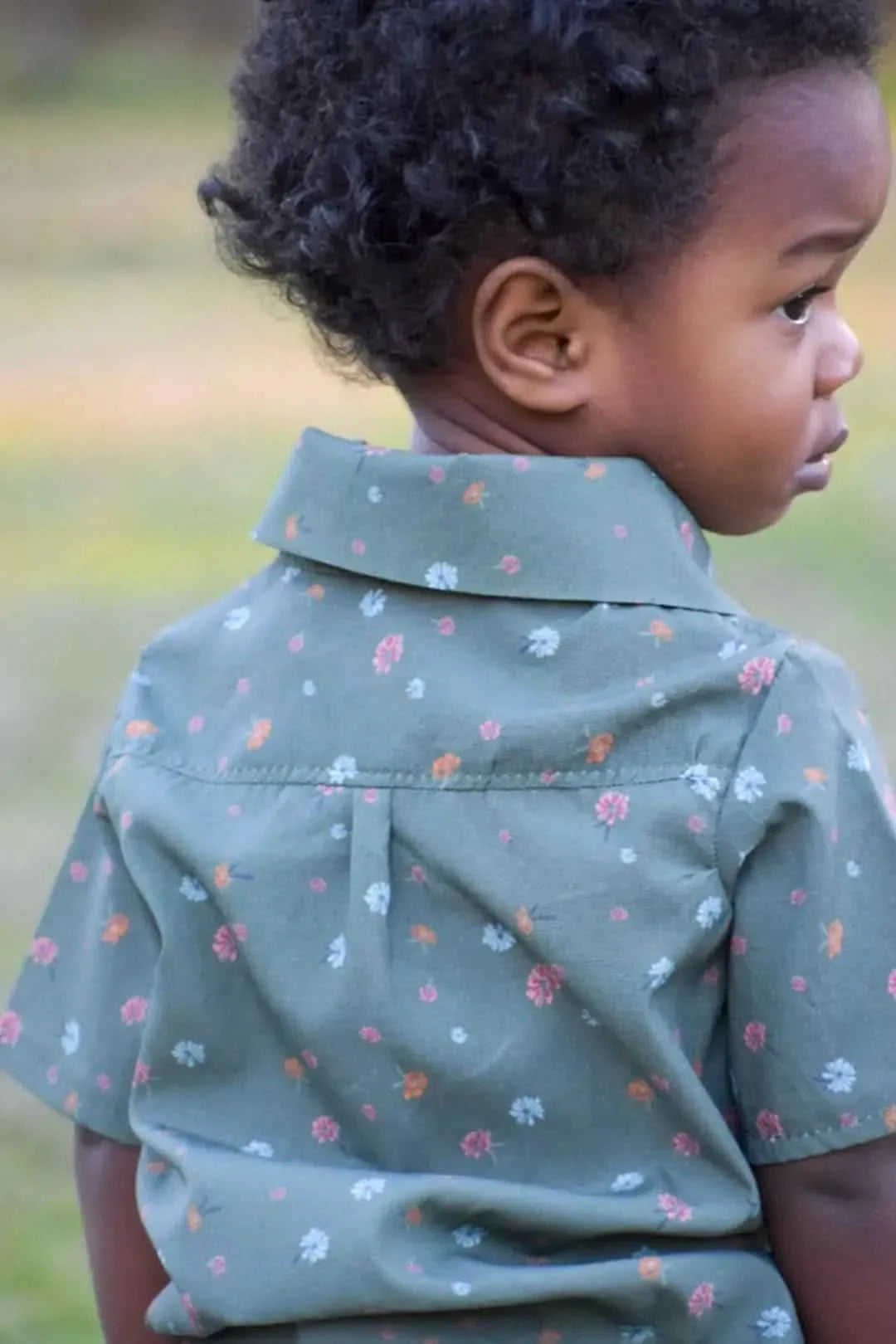 A child from behind wearing an olive floral shirt.
