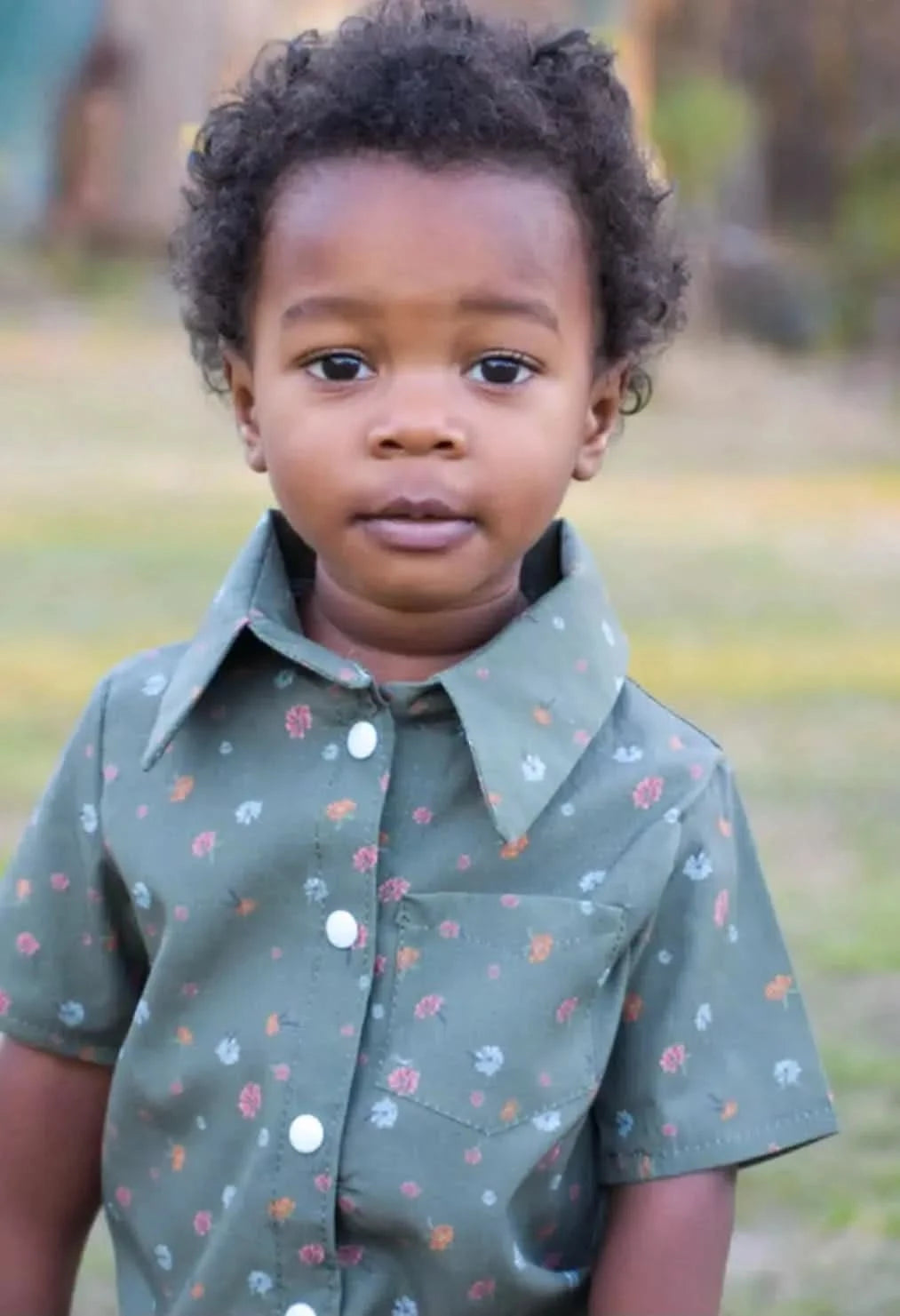 A young child wears an olive green shirt with small floral patterns.