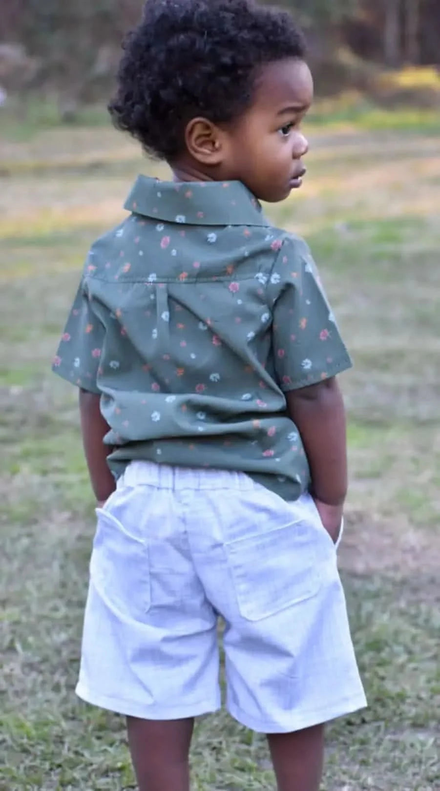 A young child in an olive floral shirt and light-colored shorts looks to the right.