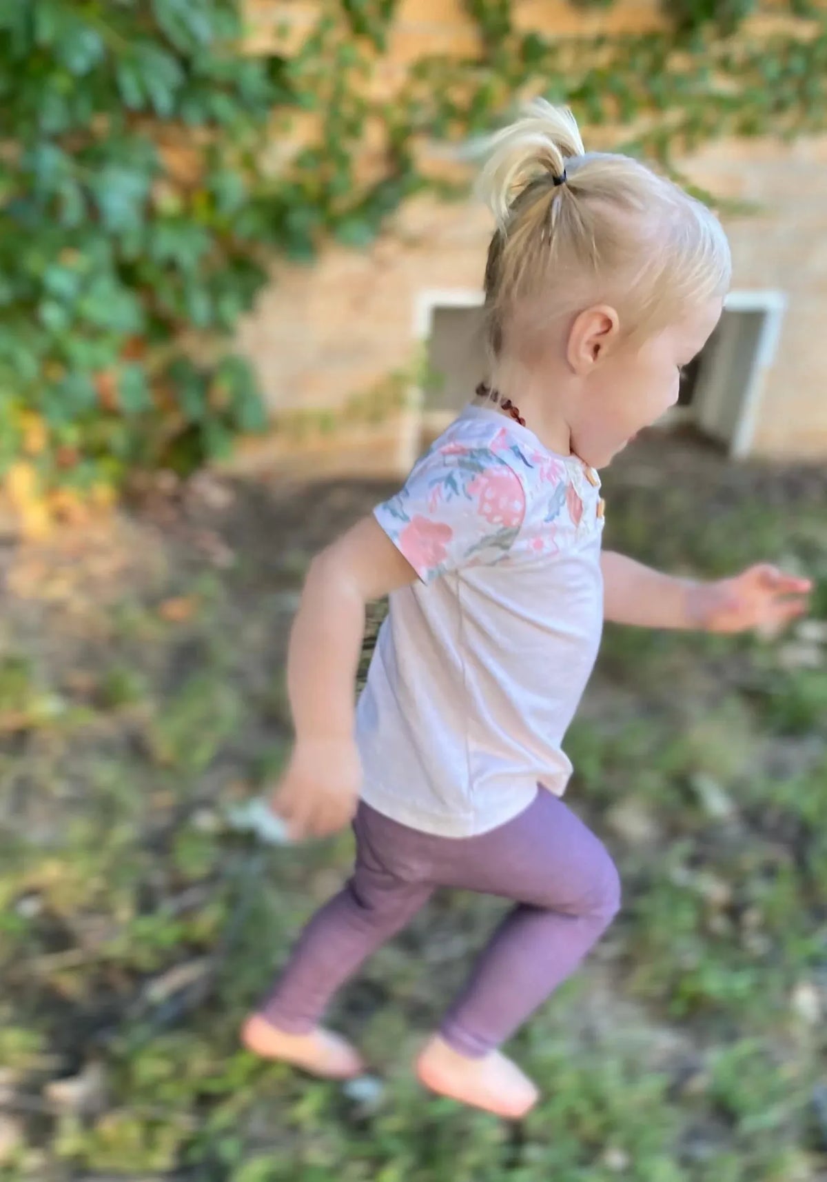 A young child in a floral shirt and purple pants runs outdoors.