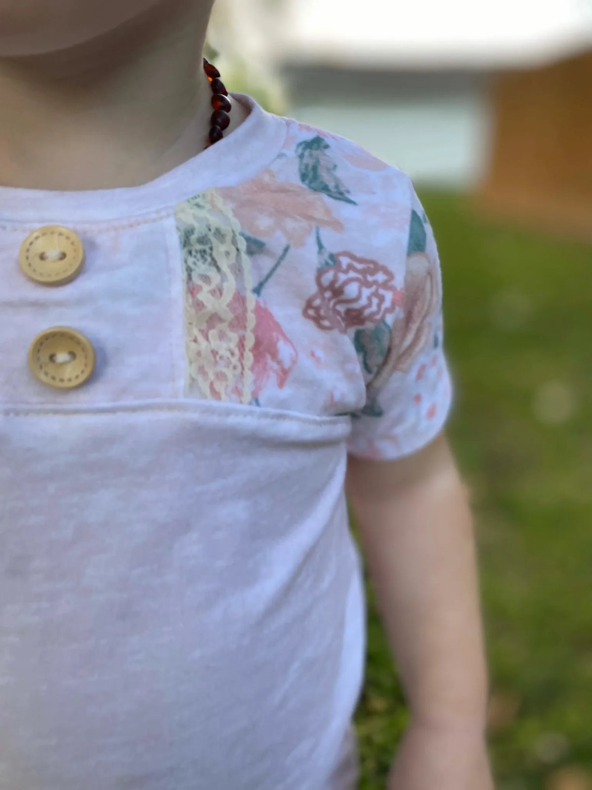 A child wears a white shirt with a floral pattern and two wooden buttons.