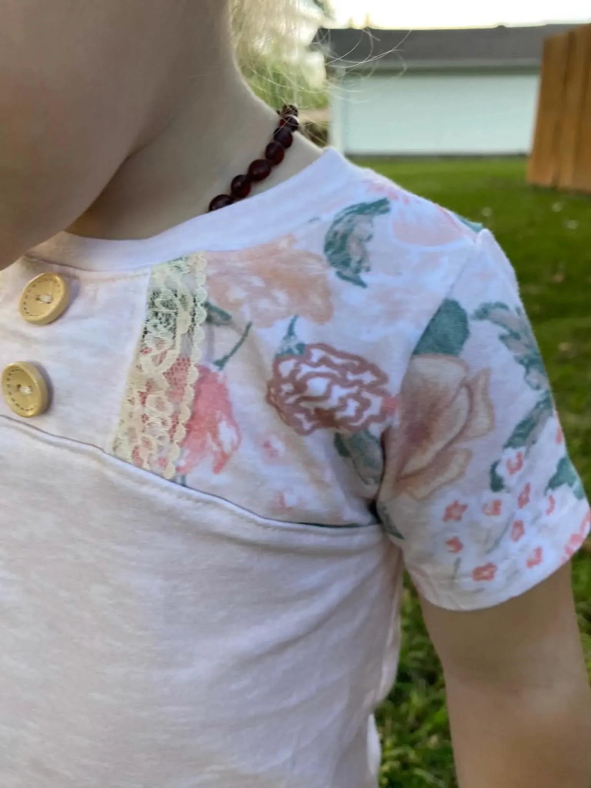 A child wears a blush floral shirt with lace trim and two buttons.