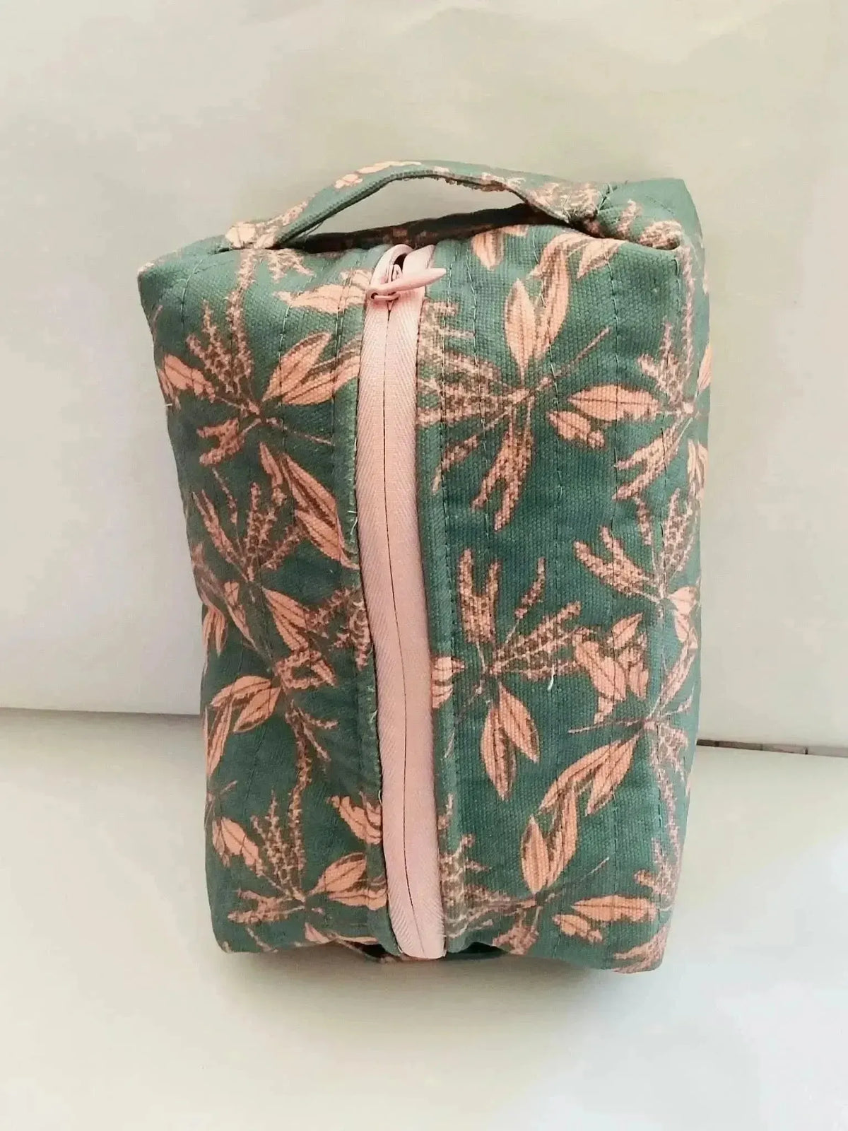 Blush hollow floral print fabric with green leaves on a pink background.