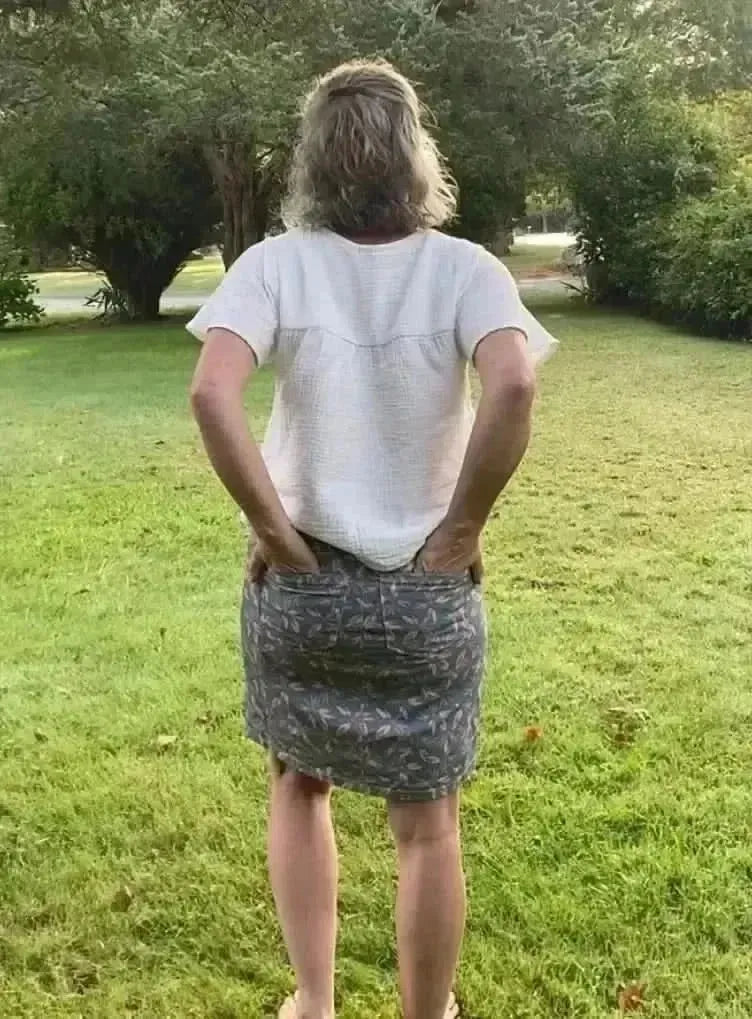 Rear view of a woman in a white short-sleeve top and blush hollow floral print skirt in a green yard.