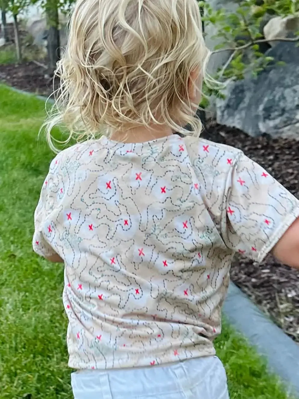 A child from behind wears a beige shirt with a red "X" map pattern.