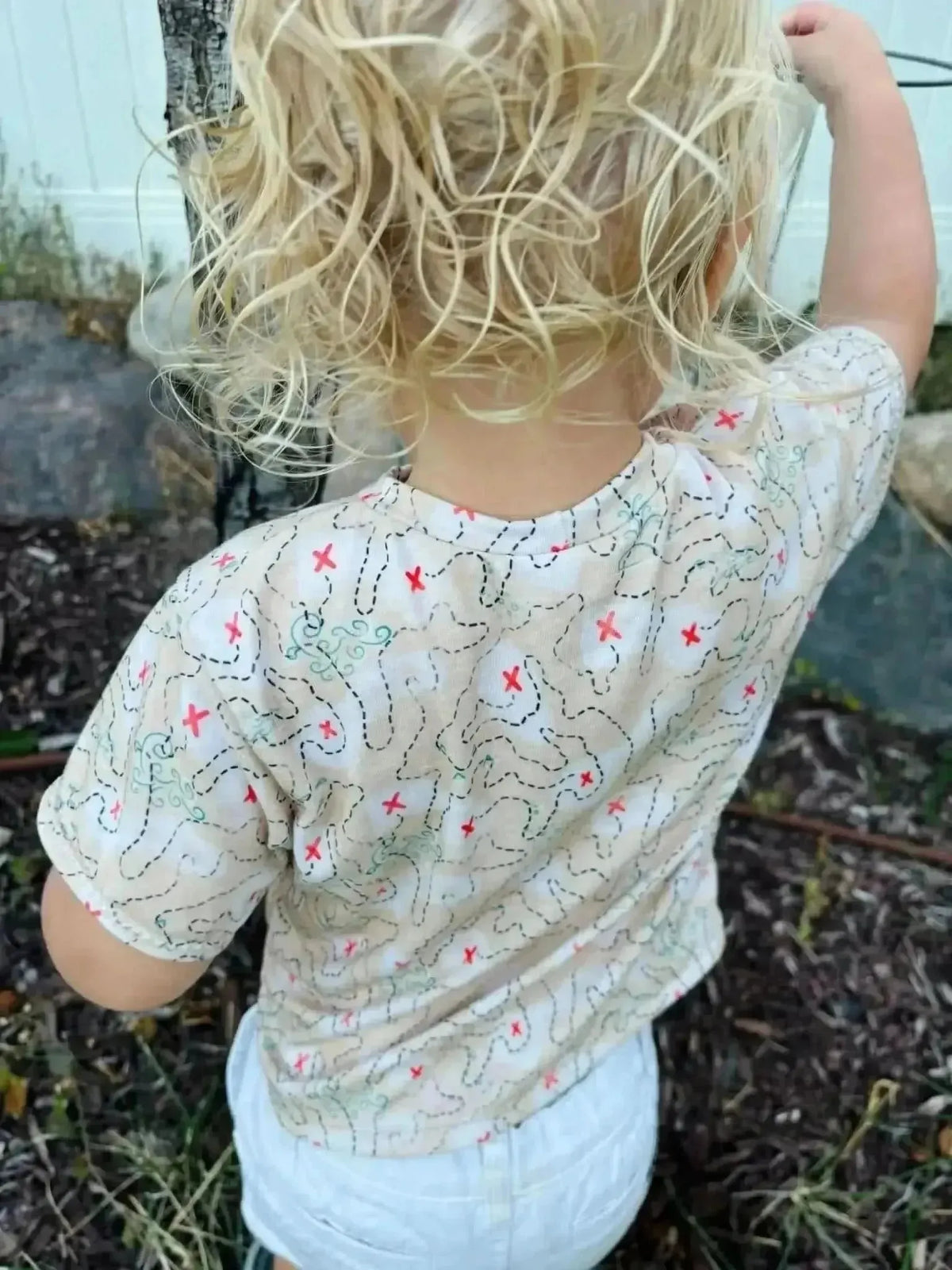 Beige fabric with red pirate map and treasure print, shown on child's shirt back.