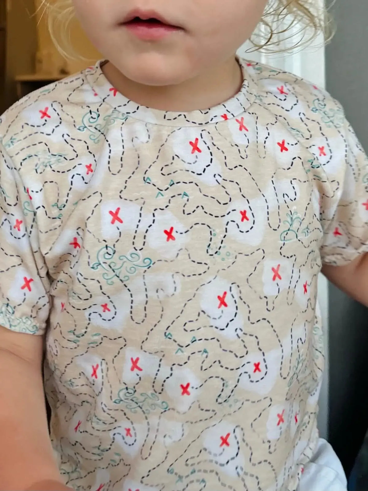 A child wears a beige t-shirt with a treasure map pattern and red X's.