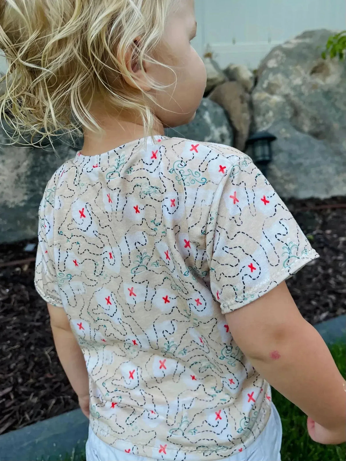 Beige fabric with red pirate map and treasure print on a child's shirt.