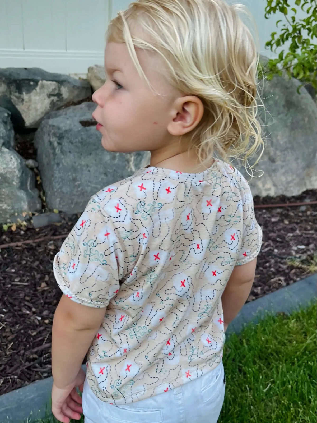 A child wears a beige shirt with a buried treasure map print.
