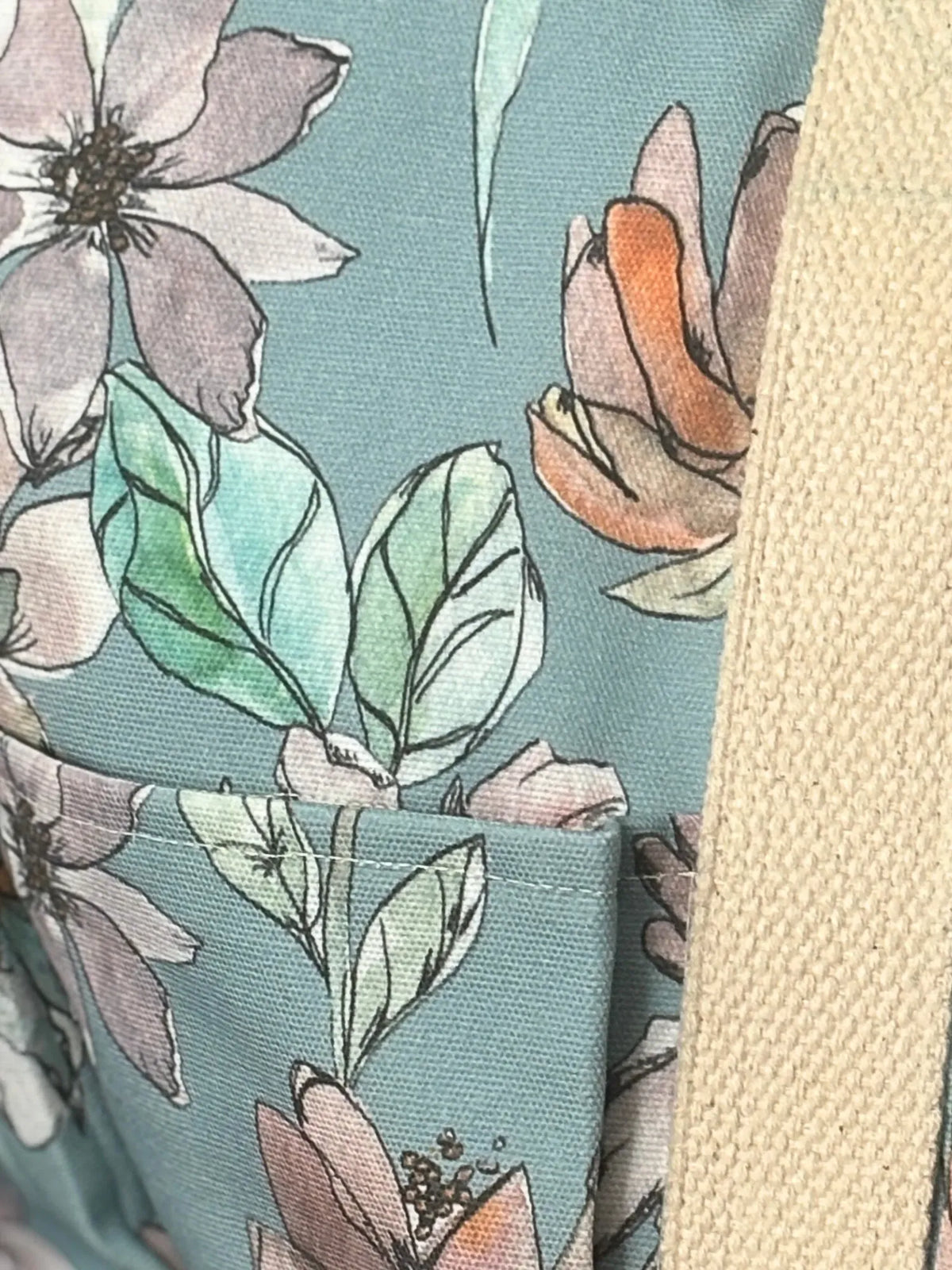 Close-up of a teal fabric with a floral pattern and a beige strap.