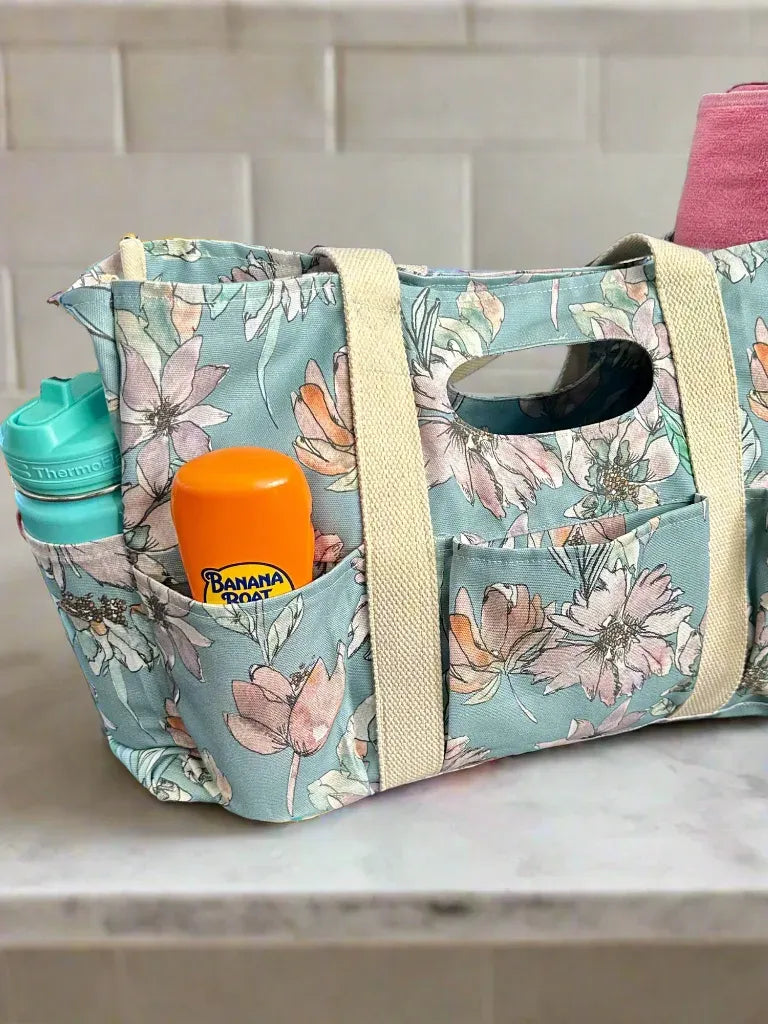 A floral tote bag with a water bottle, sunscreen, and a pink towel.
