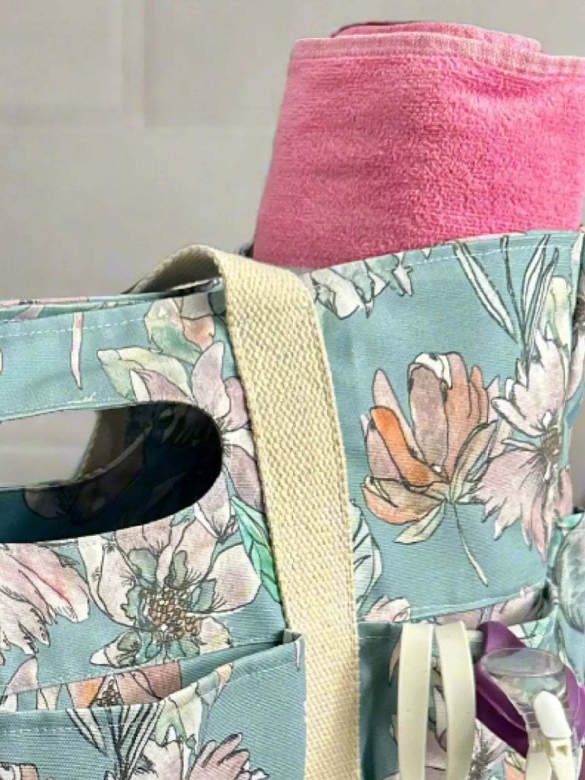 A floral tote bag with a pink towel and swim goggles.
