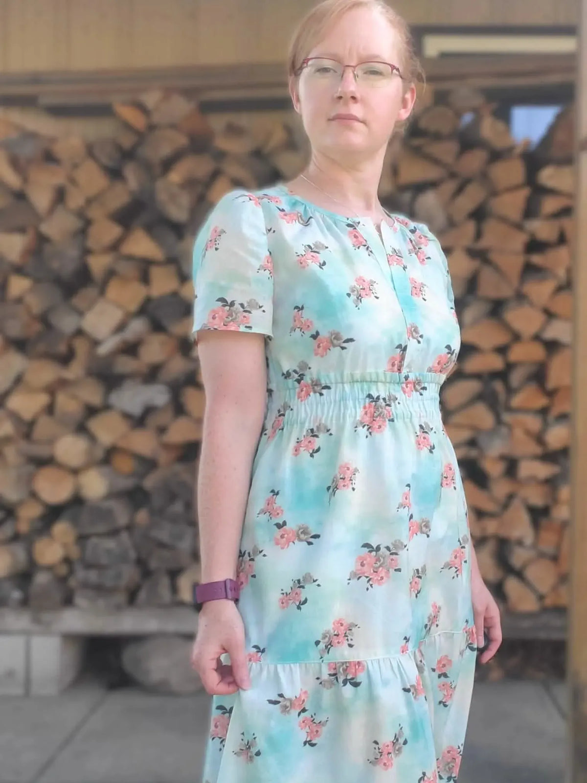 A woman wears a light blue floral dress with pink and grey peonies.