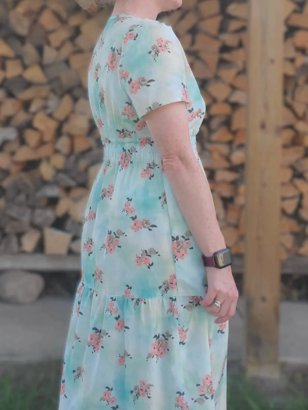 A woman in a floral dress with a shirred waist stands in profile.