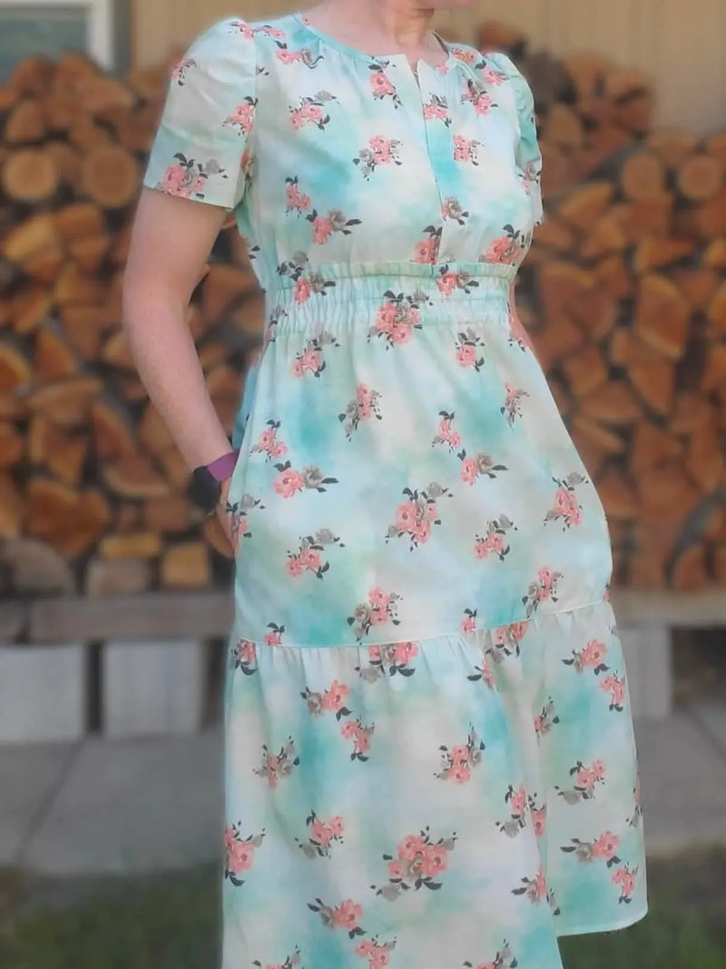 A person models a light blue floral dress with short sleeves and an elastic waist.