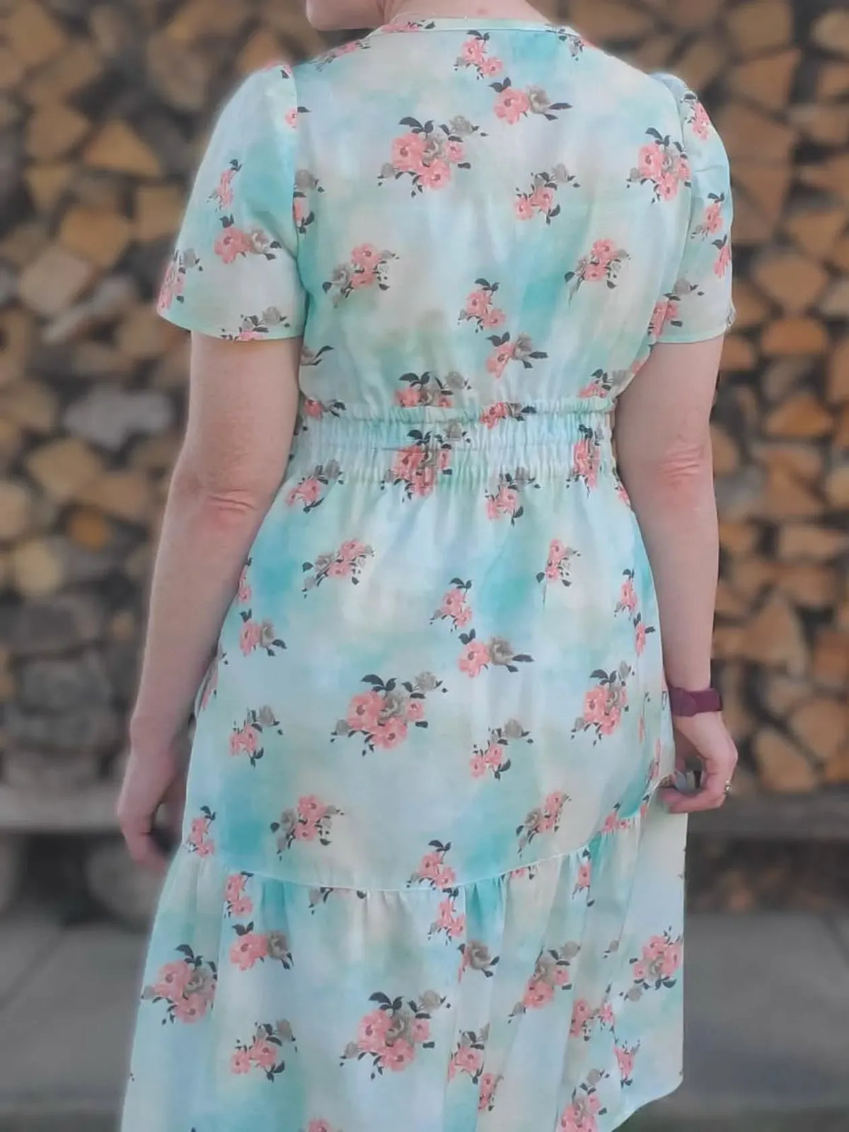 A person from behind wearing a light blue floral dress with pink peonies.