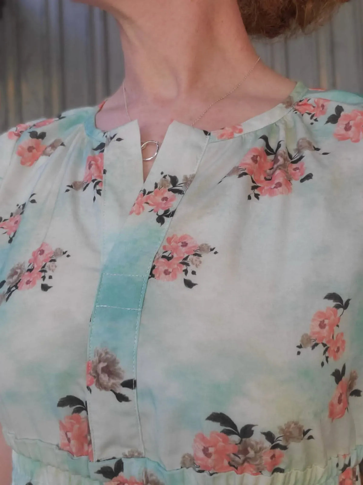 A person wears a light blue and white floral top with a silver necklace.