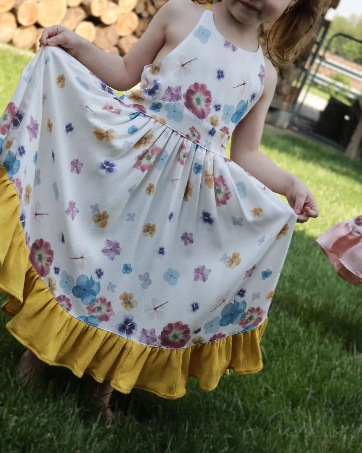 A child in a white dress with colorful pressed flowers and a yellow ruffled hem.