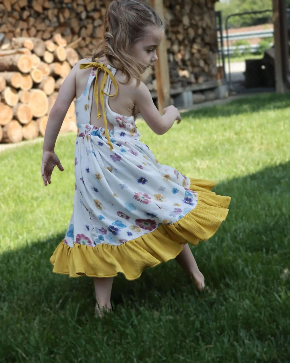 A young girl in a floral dress with a yellow ruffled hem twirls on green grass.