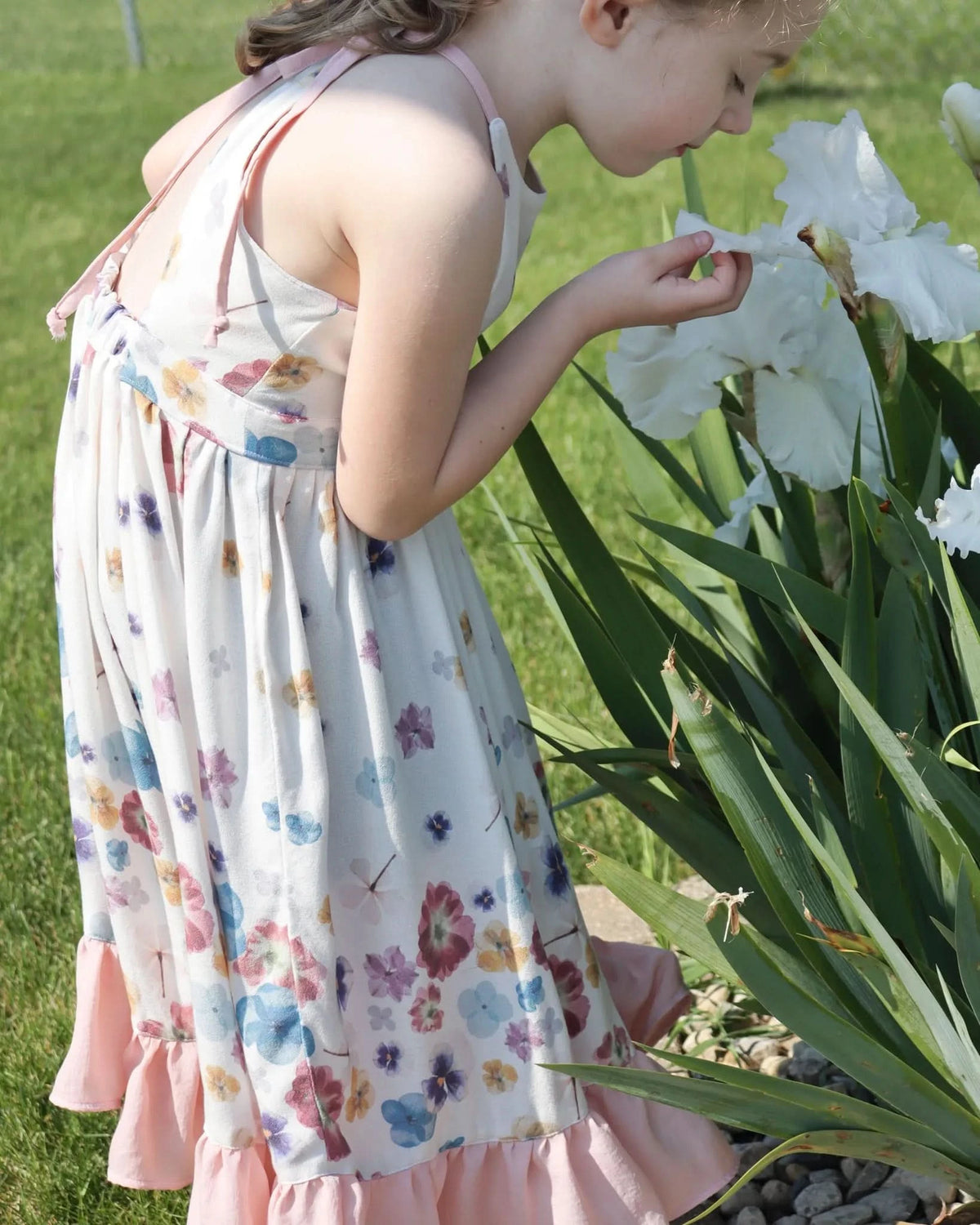 A young girl in a floral dress smells a white iris flower.