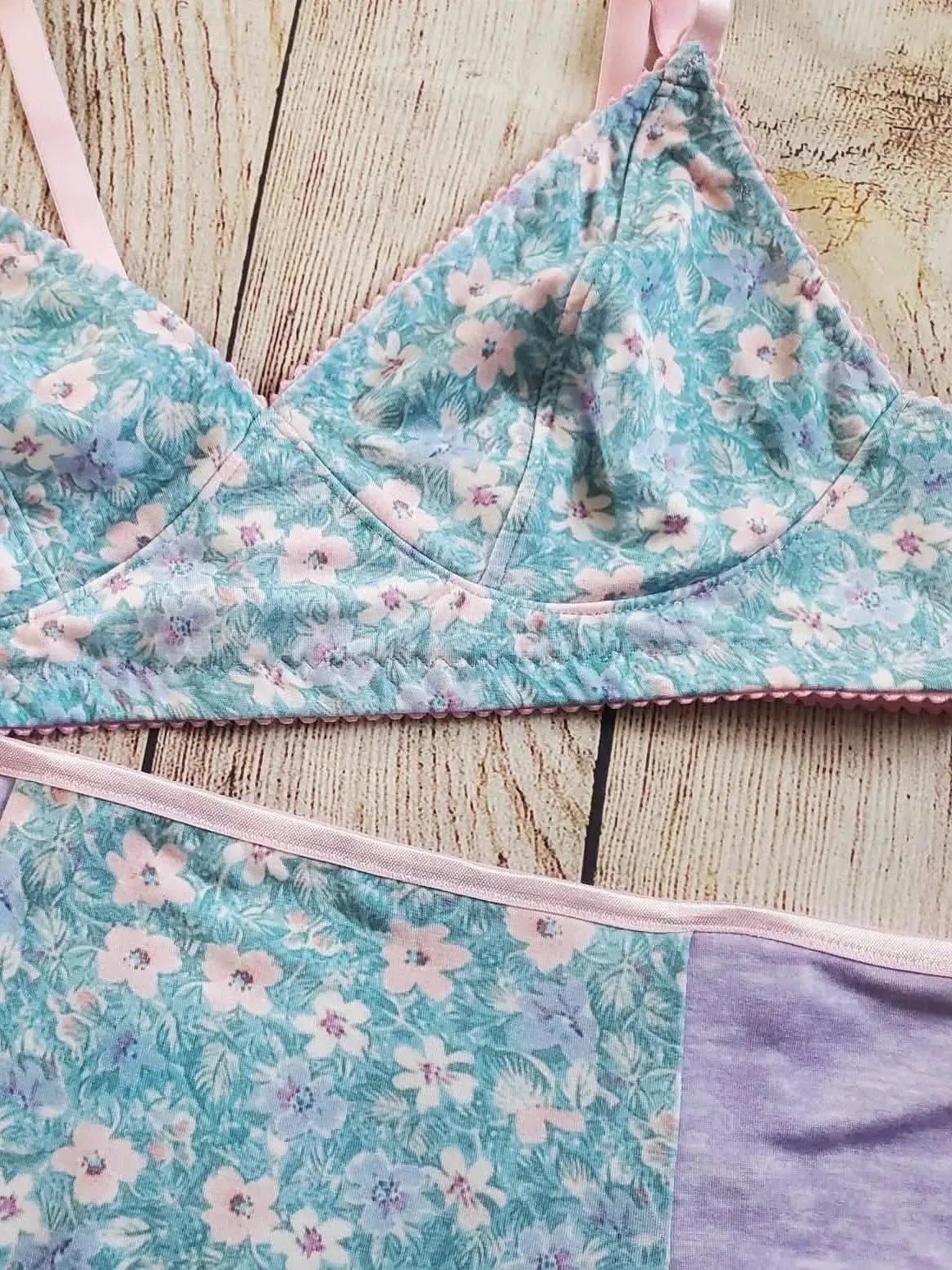 A light blue floral bra and underwear set with pink trim is displayed on a wooden surface.