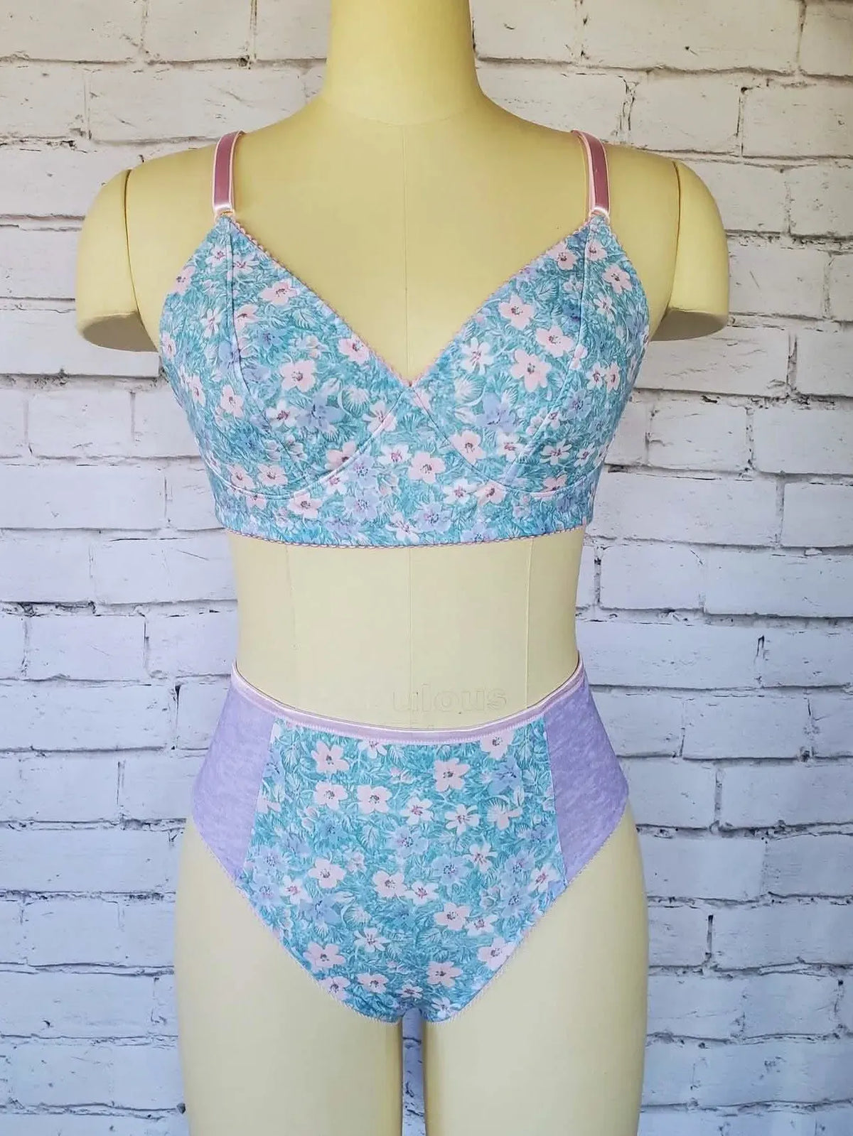 A floral bra and underwear set on a mannequin against a white brick wall.