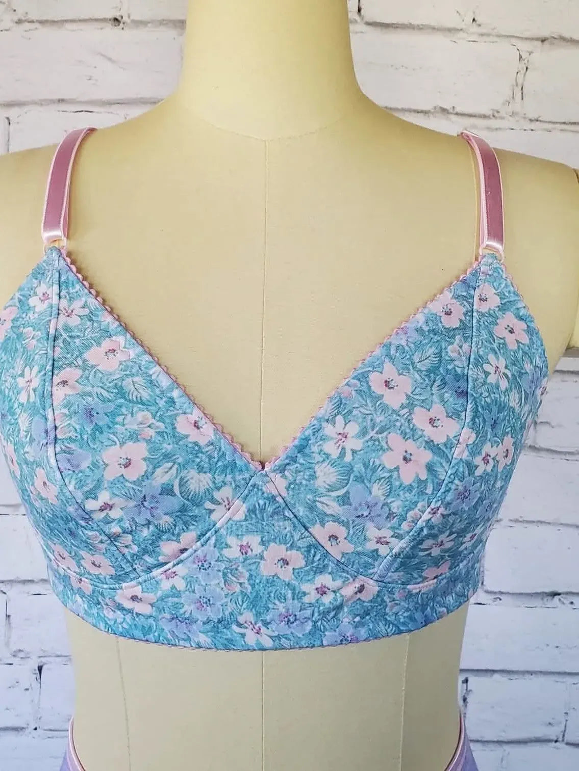 A light blue floral bra with pink straps is displayed on a mannequin.