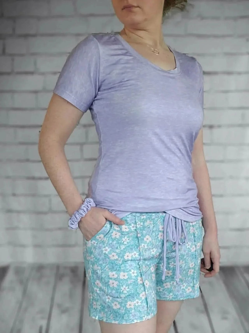 A woman wears a lilac heather t-shirt and floral shorts.