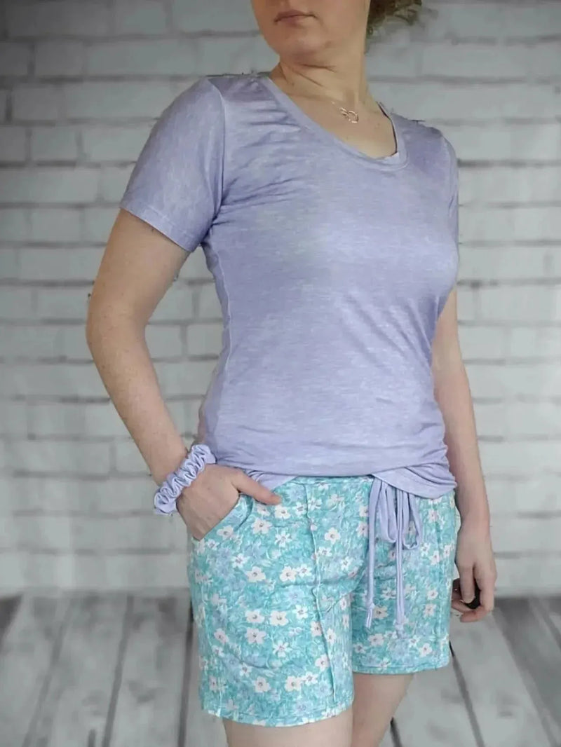 A person wears a lilac heather t-shirt and floral print shorts.
