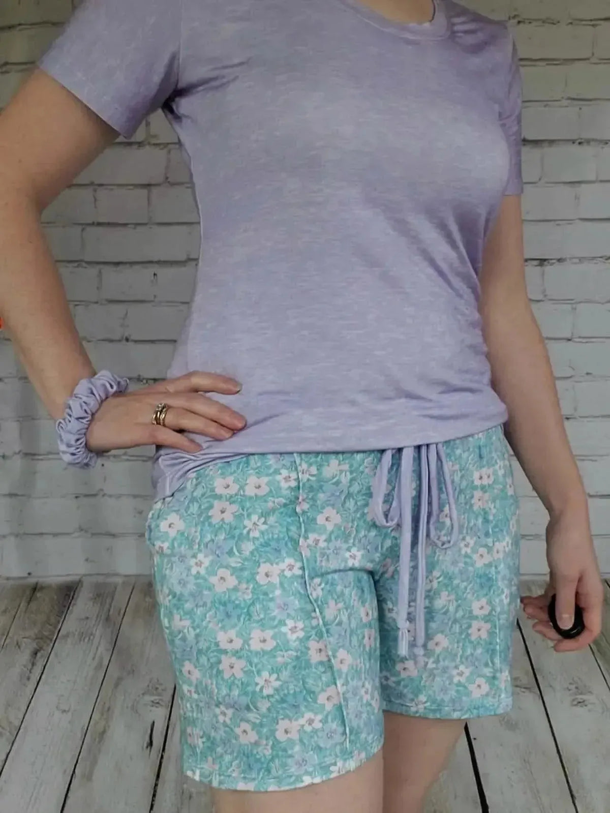 A person wears a lilac heather t-shirt and floral print shorts.