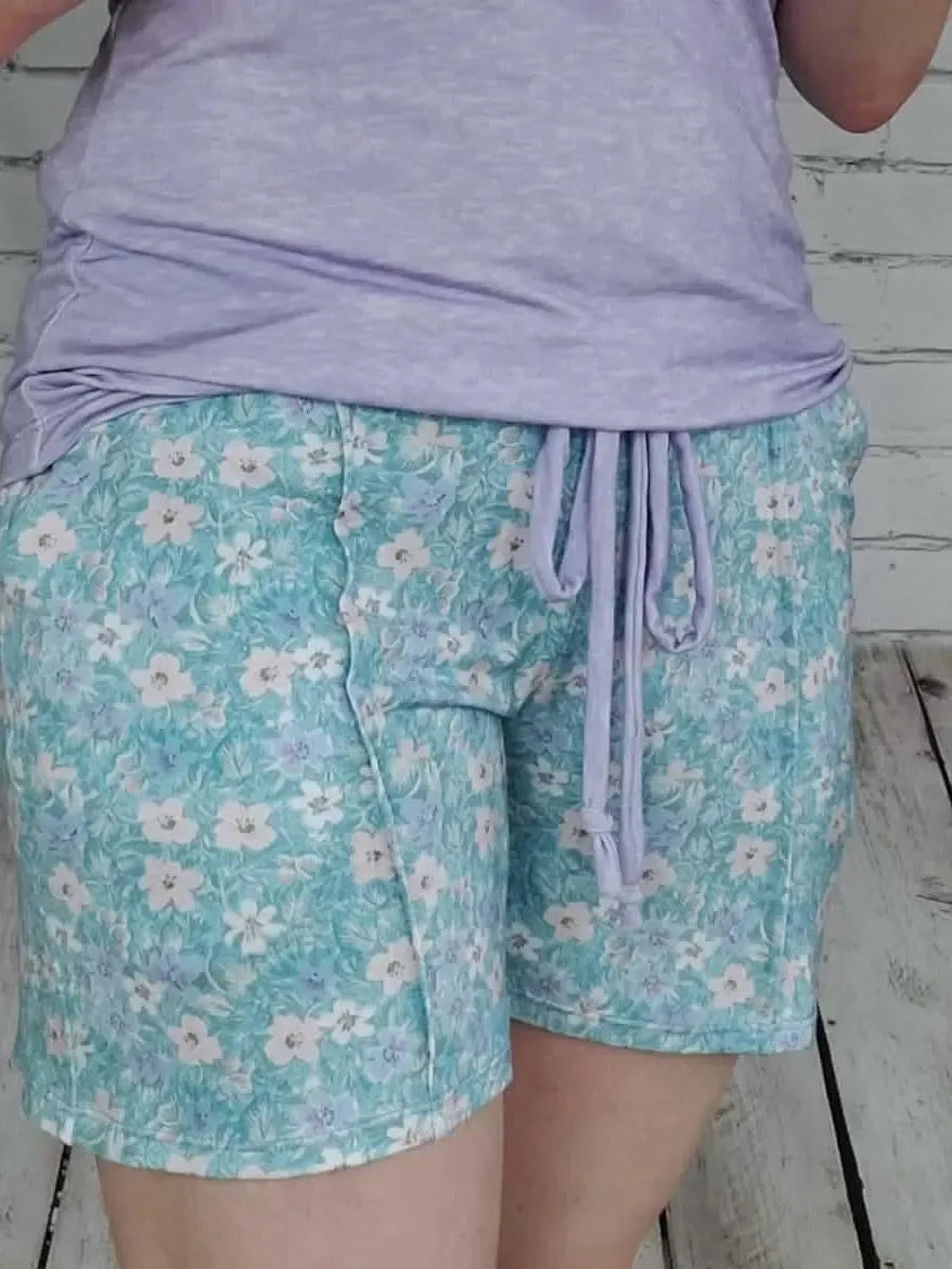A person wears light blue floral shorts with a purple drawstring and top.