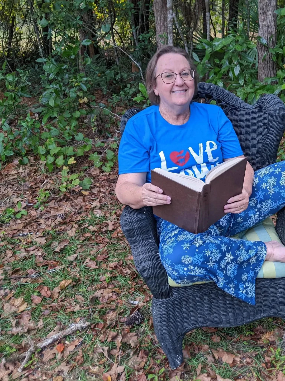 A person in blue snowflake pajamas sits in a wicker chair, reading a book.