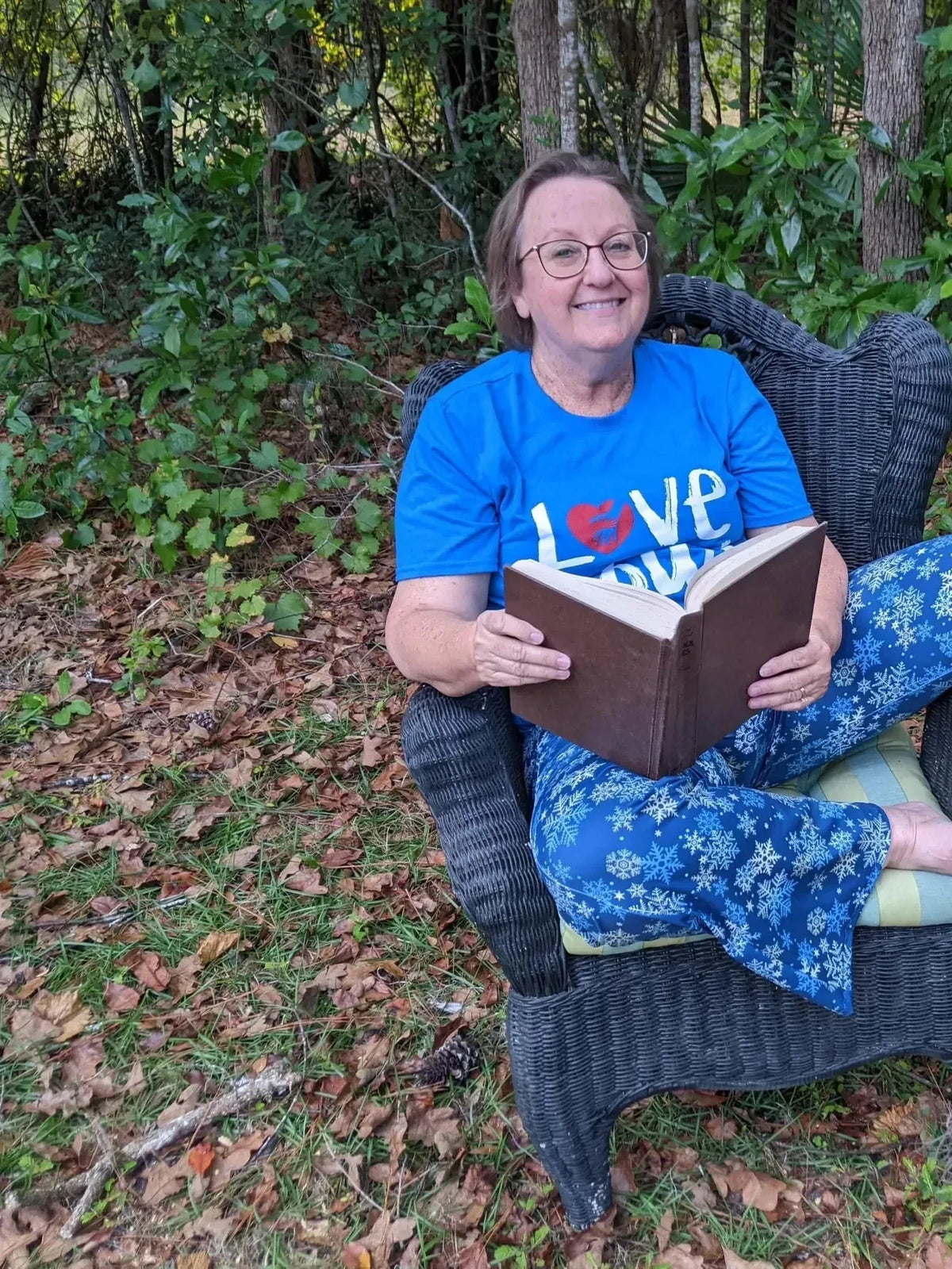 Woman lounging outdoors in blue pants with white snowflake print, reading a book.