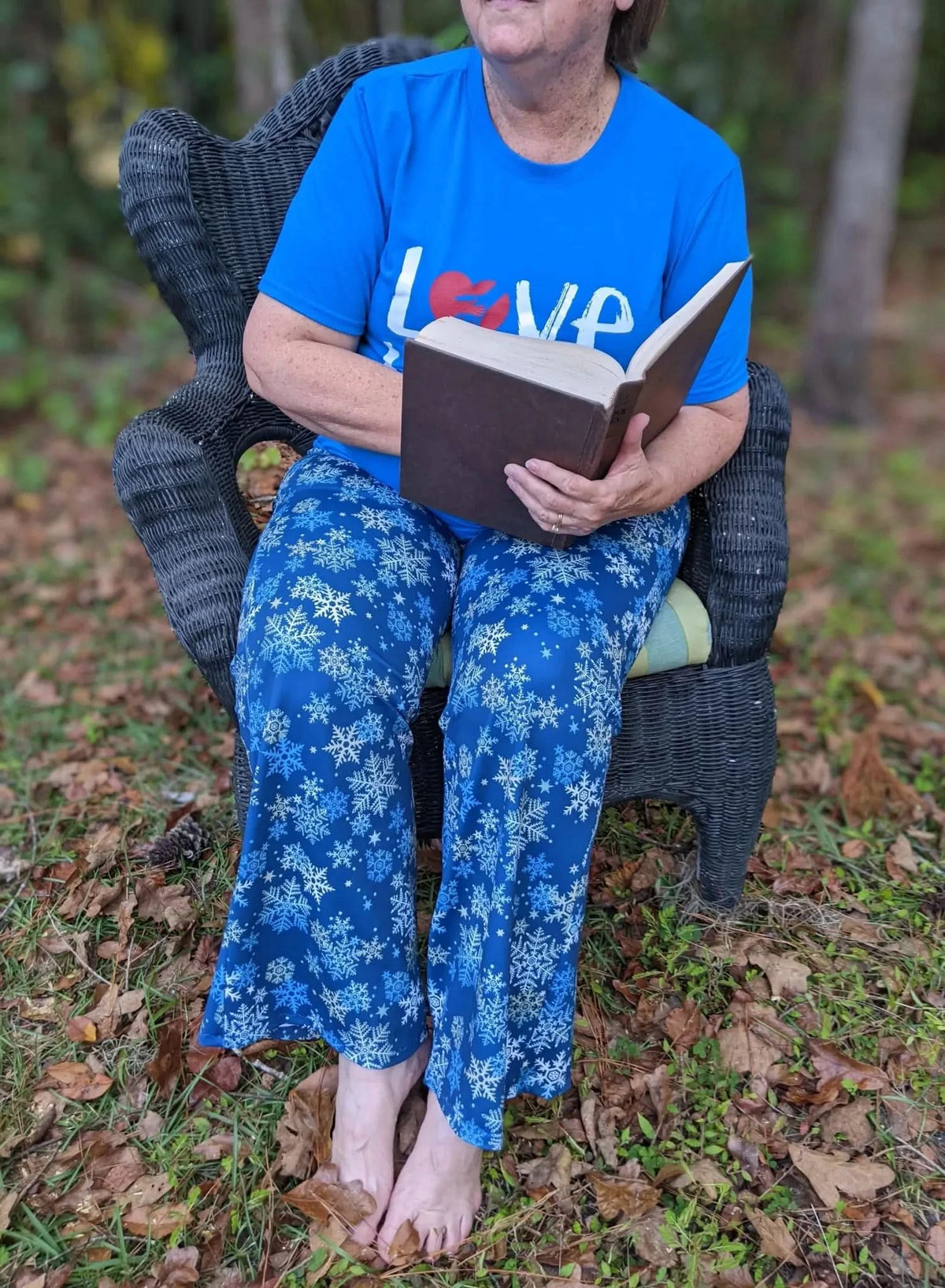 A person in blue snowflake pajamas reads a book while sitting in a wicker chair.