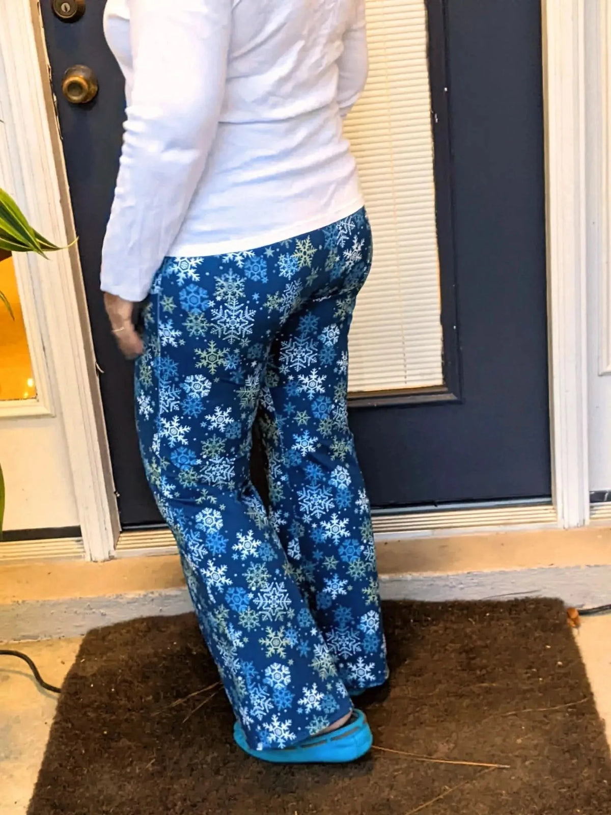 Woman wearing navy snowflake-print pants standing on a doormat outside a blue door.