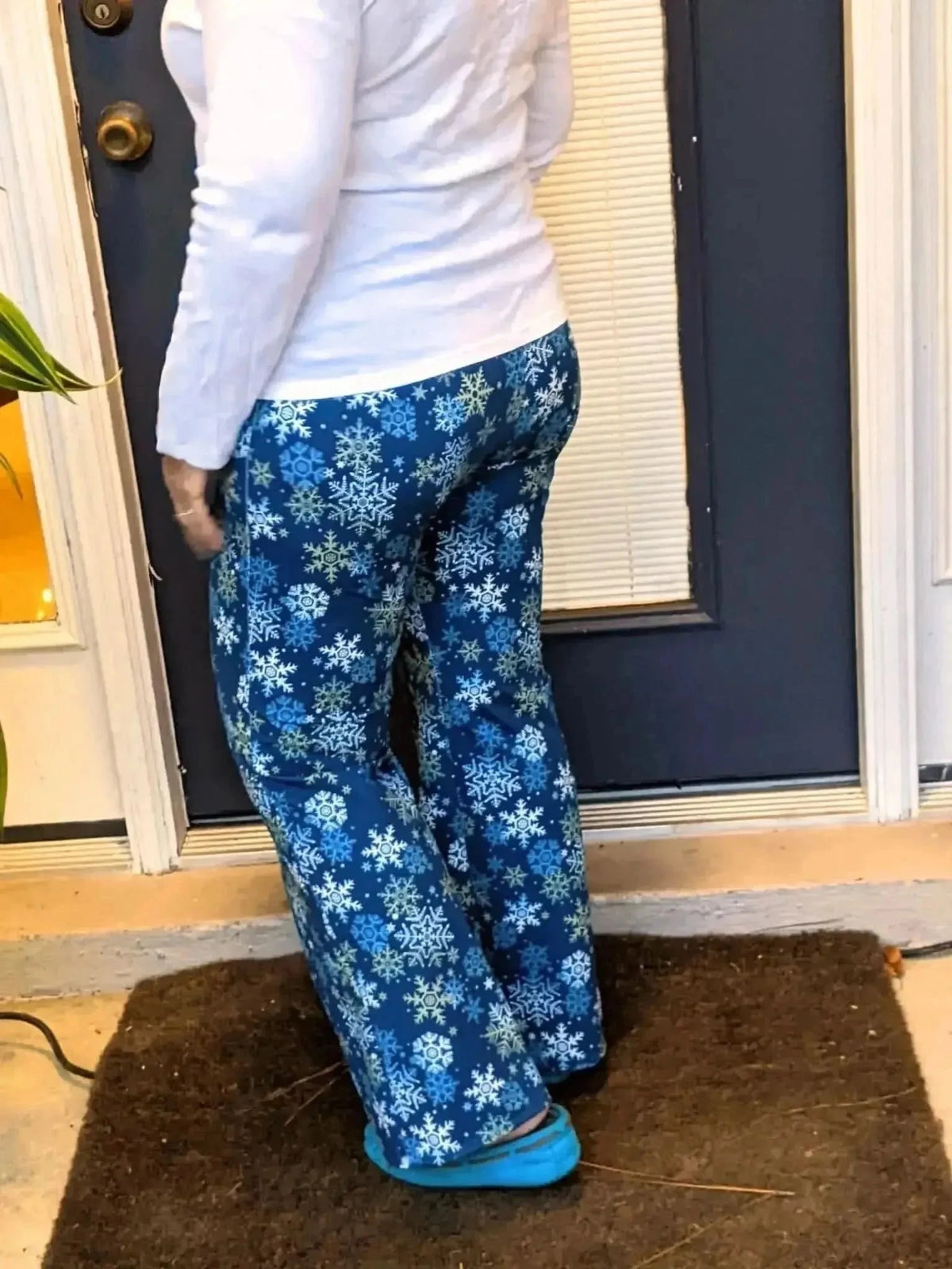Woman wearing navy snowflake-print pants standing on a doormat outside a blue door.