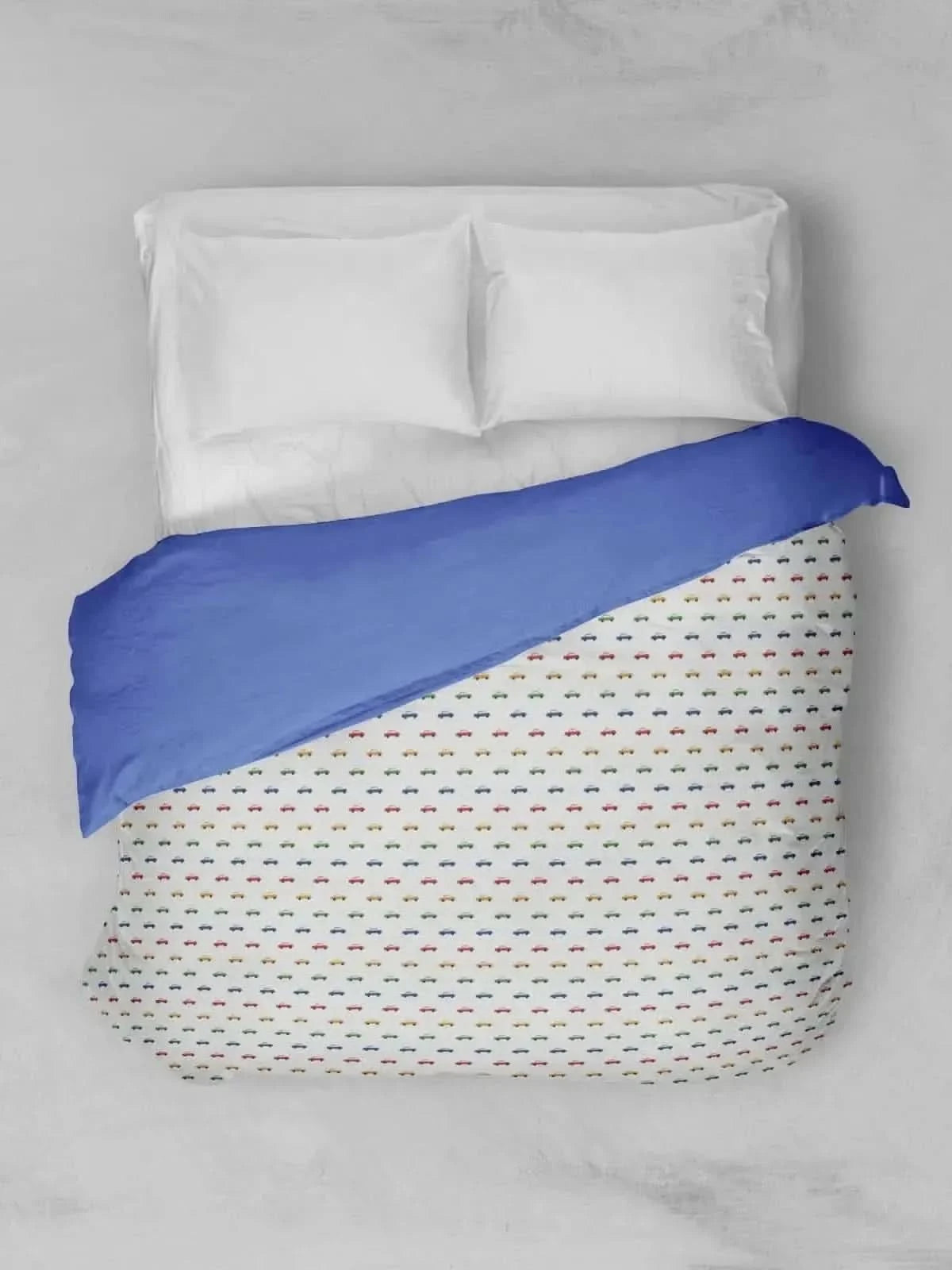 A bed with white pillows and a blue and colorful car-patterned duvet.