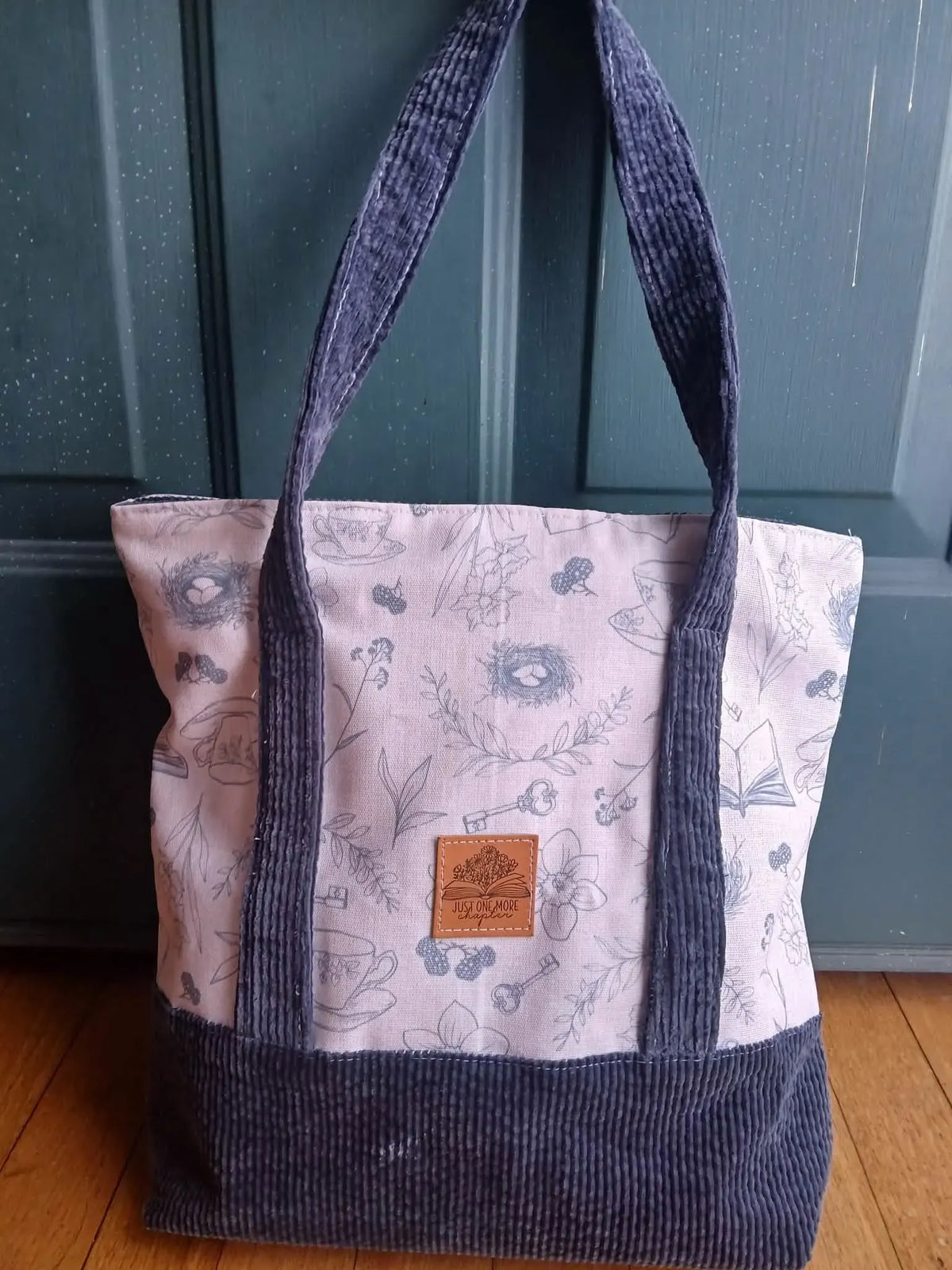 A tote bag with a light patterned top and a dark ribbed bottom.